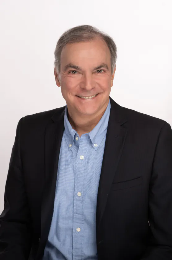 A man wearing a dark suit jacket and light blue shirt smiles at the camera.