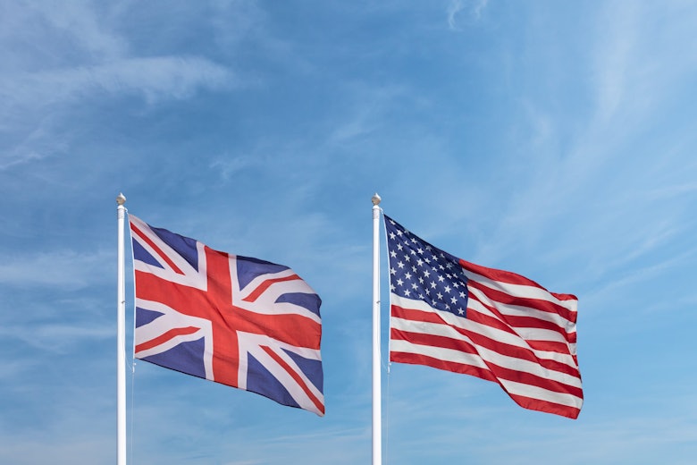 A US flag and the Union Jack, seen atop white flag poles, are seen against the backdrop of a blue sky.