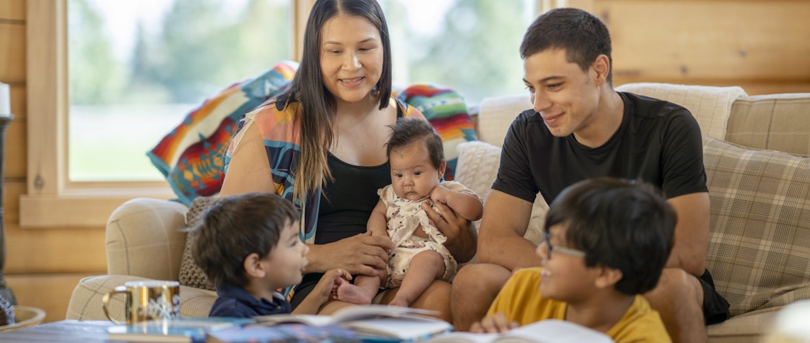 An Indigenous mother and father smile at their three young children.