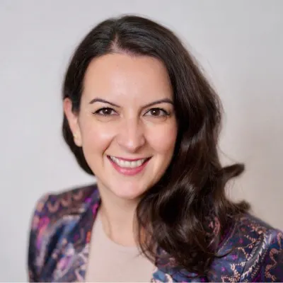 A woman with long dark hair pulled over one shoulder smiles at the camera.