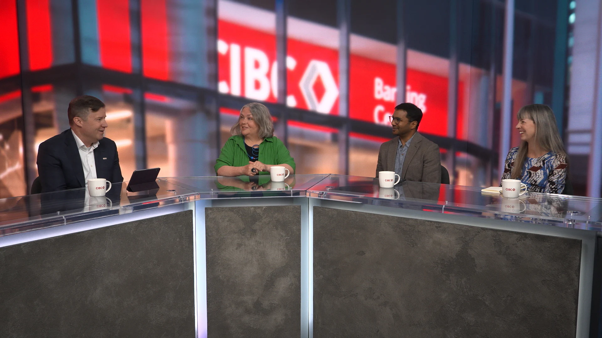 Four people sit behind a desk, with three on the right turning to look at the person on the left. The CIBC logo is on the wall behind them.