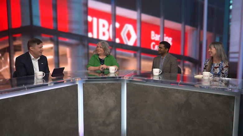 Four people sit behind a desk, with three on the right turning to look at the person on the left. The CIBC logo is on the wall behind them.