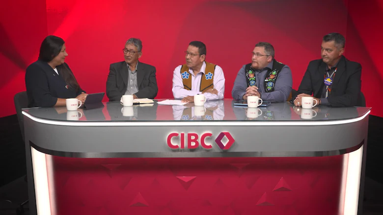 Four men sit behind a desk with the CIBC logo at front and centre, with a red wall behind them. They are all looking at a woman to the left of the image.